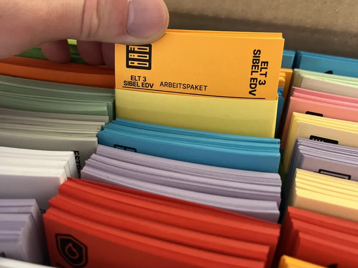 Versandfertige Pakete mit bunten Lean-Steckkarten - Einfache Entnahme und Organisation für das tägliche Stand-up-Meeting.